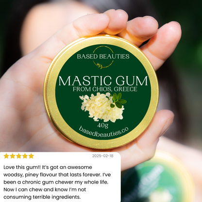 Hand holding a container of mastic gum with a green label, featuring the brand 'Based Beauties'.